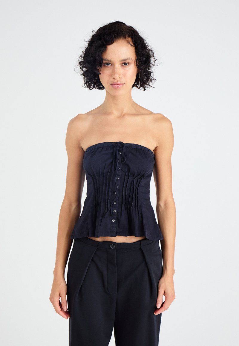 Σκούρος μπλε τοπ χωρίς μανίκια με συγκεντρωμένο σχέδιο, διαθέτει κουμπί μπροστά και δεμένη λαιμόκοψη. Λείο υλικό και εφαρμοστή γραμμή.