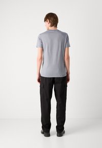 Light gray short-sleeve shirt made of cotton blend, fitted design. Paired with black cargo pants featuring large side pockets and cuffed hems.