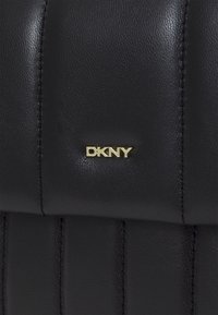 Czarna skórzana torebka z pionowym pikowanym wzorem, złotą plakietką z logo "DKNY" i gładką teksturą. Posiada tonowane przeszycia dla detalu.
