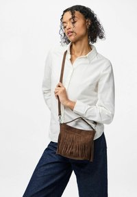 Brūna zamša crossbody soma ar frizieriem, īsu rokturi un garu regulējamu siksnu. Somai ir gluda tekstūra.