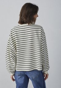 Stribet cremet og marineblå pullover med en afslappet pasform, der har ballonærmer og ribbede manchetter, parret med blå denim jeans.