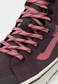 Lilla semsket høyhælte sko med rosa mønstrede snorer, svarte hull og rosa sidestripe. Hvit gummisåle med teksturerte detaljer.
