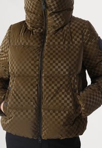 Brun ternet dunjakke med høj krave, frontlynlås og lommer med knappelås. Glinsende tekstur med sorte detaljer.