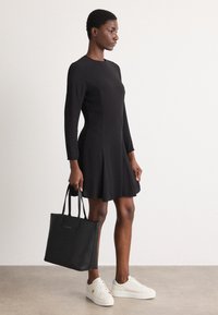 Melnās garās piedurknes kleita ar platu svārku, apvienota ar baltām sporta kurpēm un melnu rokassomu. Gluda auduma, vienkāršs dizains, bez rakstiem.