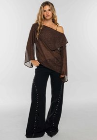 Top de lentejuelas bronce con diseño asimétrico y mangas largas, combinado con pantalones negros de pierna ancha con tachuelas plateadas a lo largo de los costados.