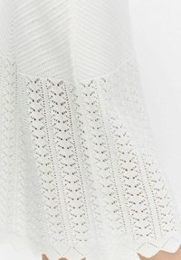 Jupe en tricot blanc avec une partie supérieure texturée ornée de rayures horizontales et d'un motif de dentelle détaillé à l'ourlet. Design à bord festonné.