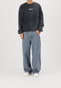 Tummanharmaa oversize-mallinen collegepaita pyöreällä pääntiellä, jossa valkoiset tekstit "MOONLIGHT ROMANCE." Yhdistetty vaaleansinisiin leveälahkeisiin farkkuihin ja valkoisiin tennareihin.