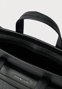 Fekete bőr válltáska texturált anyaggal, masszív vállpántokkal és dombornyomott logóval. A belső tere tágas, sima felülettel.