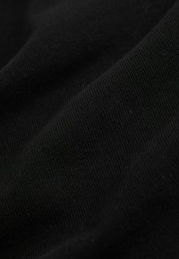 Fekete bordázott szövet közeli képe, amely finom kötésmintát és lágy redőket mutat.