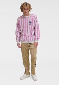 Rosa och grå randig sweatshirt med ribbad krage, med en logotyp på bröstet; matchad med beige mönstrade byxor och vita sneakers.