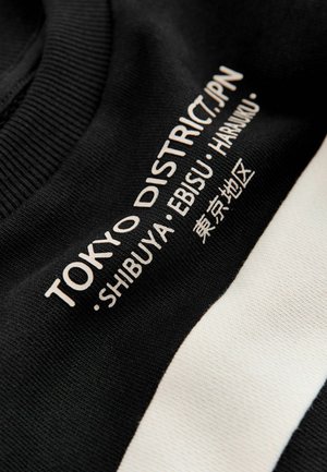 Hanorac negru cu dungi orizontale albe, având text imprimat "TOKYO DISTRICT.JPN - SHIBUYA - EBISU - HARUMI" într-un font modern.