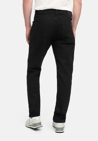 Vaqueros de mezclilla negros con corte slim, que cuentan con cinco bolsillos y detalles de costura sutiles. Llevados con zapatillas de color claro.