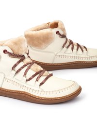 Botas de cuero beige con un suave cuello de piel sintética color marrón, cordones marrones y costuras en contraste, montadas sobre una suela de goma.