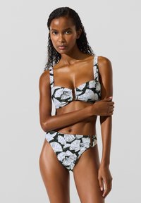 Mustvalge bikiinikomplekt troopilise lehe mustriga, millel on struktureeritud top laiade rihmadega ja kõrgvöökohaga püksid metalldetailidega.