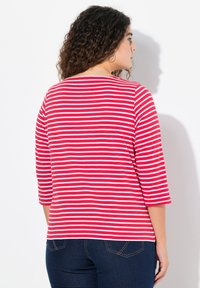 Gestreiftes Shirt in Rot und Weiß mit Dreiviertelärmeln, Rundhalsausschnitt und weicher Textur, kombiniert mit dunkelblauen Jeans.