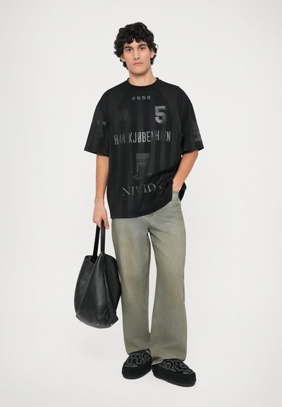 Czarny, oversize t-shirt z graficznymi nadrukami i fakturami, zestawiony z jasnorozowymi spodniami o prostym kroju i czarną torbą. Akcesoria to czarne buty.