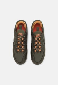 Mörkgröna Nike Air-sneakers med en texturerad överdel, orange detaljer och platta snören. Den inre foder är orange med en vadderad krage.