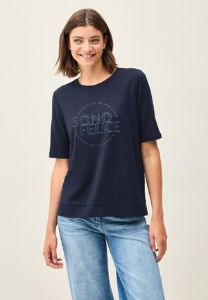 T-shirt bleu marine à manches courtes en tissu doux, avec un design imprimé circulaire de texte « SONO FELICE » en bleu clair. Texture lisse.