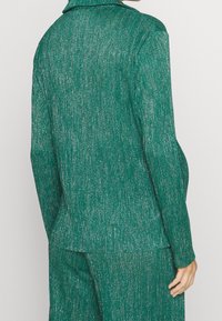 Grön tweedblazer med glänsande metallfibrer, skräddarsydd passform, skarp krage och mjuk textur, stylad med matchande byxor.