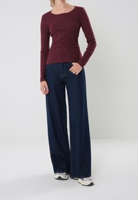 Burgundy ribbed long-sleeve top paired with high-waisted, wide-leg dark denim jeans. Footwear includes light-colored sneakers.