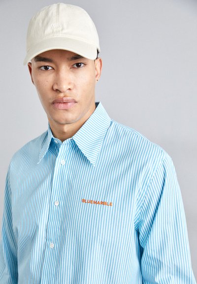 Camisa de botón a rayas azul claro con un gran cuello y bordado en naranja "BLUEMARBLE". Presenta botones blancos y una textura de tela suave.