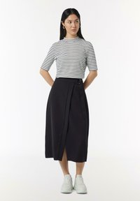 Zwarte wikkelrok met riemdetails, gecombineerd met een korteblauwe witte blouse met horizontale zwarte strepen. Witte sneakers maken de outfit compleet.