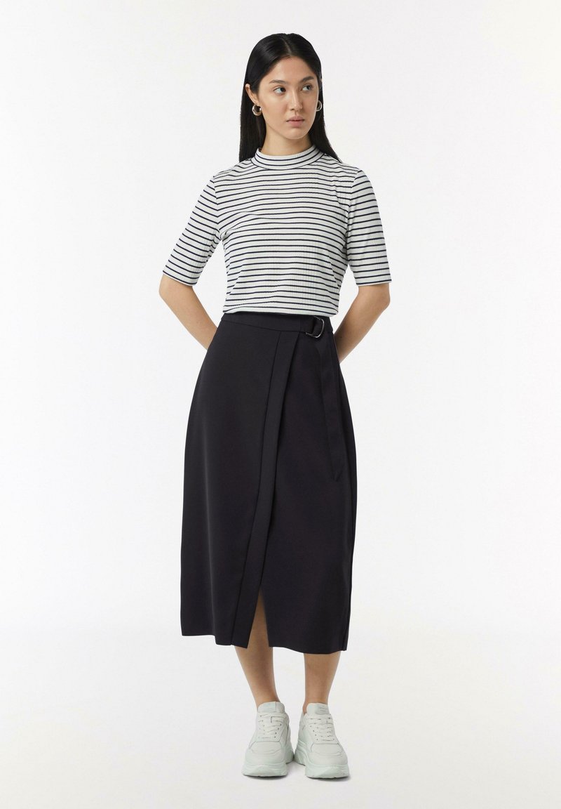 Zwarte wikkelrok met riemdetails, gecombineerd met een korteblauwe witte blouse met horizontale zwarte strepen. Witte sneakers maken de outfit compleet.