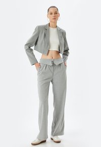 Blazer gris de corte cropped con rayas sutiles, combinado con pantalones grises de cintura alta que tienen una original cinturilla con doble pliegue y cierre de dos botones.