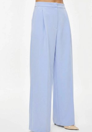 Pantaloni azzurri chiaro a vita alta e gamba larga con pieghe frontali e tasche laterali, indossati con tacchi beige a punta su sfondo bianco.