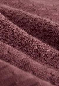 Gros plan d’un tissu doux et texturé avec un motif en gaufrage nid d’abeille de couleur mauve atténuée, montrant des plis et de la profondeur.