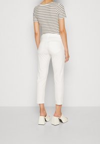 Striped gray and cream short-sleeve top, paired with white ankle-length pants and block-heeled mules, viewed from the back.