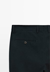 Dunkelblaue Baumwollhosen mit einer Gesäßtasche mit einem einzelnen braunen Knopf, Gürtelschlaufen und einer glatten Textur.