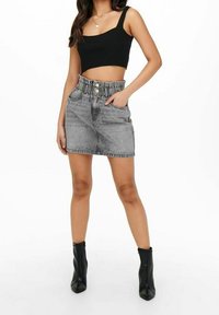 Grauer Denim-Minirock mit elastischem Bund, zwei Fronttaschen und Knopfverschluss. Getragen mit einem schwarzen gerippten Crop-Top und schwarzen Knöchelstiefeln.