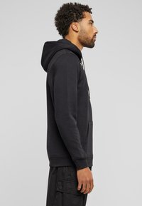 Felpa nera con cappuccio realizzata in cotone, dotata di tasca frontale, coulisse e polsini a coste. Design semplice con una vestibilità comoda.