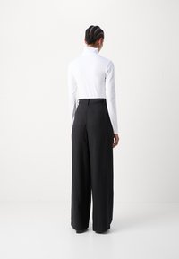 Pitkähihainen valkoinen paita korkean kauluksen kanssa, yhdistettynä leveälahkeisiin mustiin housuihin, joissa on kaksi takataskua ja sileä pinta.