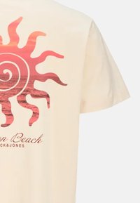 Beige cotton t-shirt featuring a large pink sun graphic with swirling rays, and the text "On Beach" and "Jack & Jones" in a simple font.