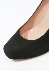 Czarne zamszowe szpilki z okrągłym noskiem i niskim wycięciem. Wnętrze ma gładką jasną podszewkę.