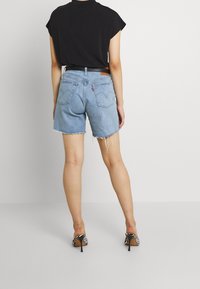 Celana pendek denim berwarna biru muda dengan ujung frayed, pinggang tinggi, dan saku belakang. Dipasangkan dengan atasan hitam dan sepatu hak tinggi bermotif zebra.