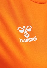 Pomarańczowy sportowy strój z gładkiego materiału, z białym logo "hummel" oraz wzorem przypominającym pszczołę z przodu.
