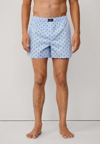 Svijetloplave muške bokserice s uzorkom malih tamnih oblika, elastičnu waistband i prednje dugme. Pamuk s glatkom teksturom.