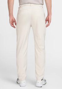 Svetlo bež hlače z gladko teksturo, dvema zadnjima žepoma in naravnim krojem nog. Obute so z belimi športnimi čevlji.