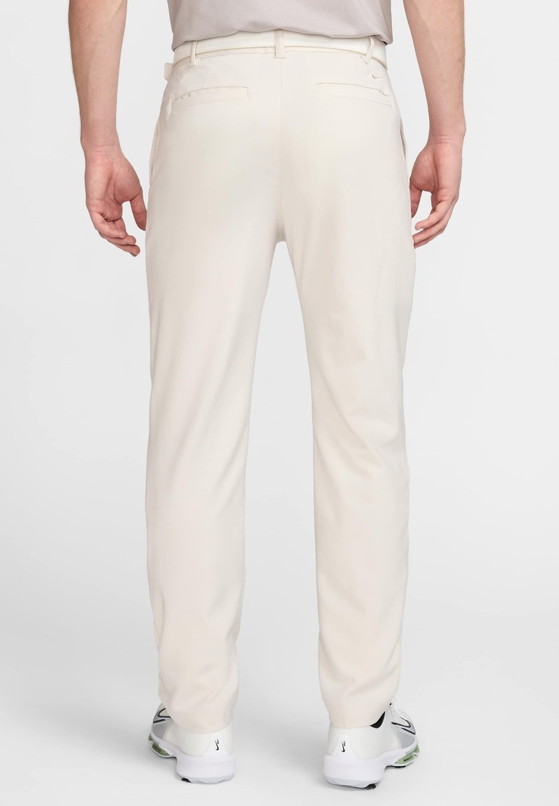 Hellbeige Hose mit glatter Textur, zwei Gesäßtaschen und geradem Bein Design. Getragen mit weißen Sportschuhen.