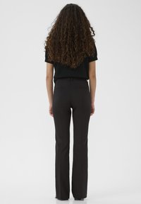 Black flared pants with a tailored fit, smooth texture, and belt loops. Cut falls to the feet, featuring two back pockets.