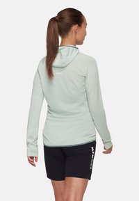 Ljus mintgrön hoodie med långa ärmar, texturerat mönster och logotyp på ryggen. Parat med svarta shorts med vit branding.