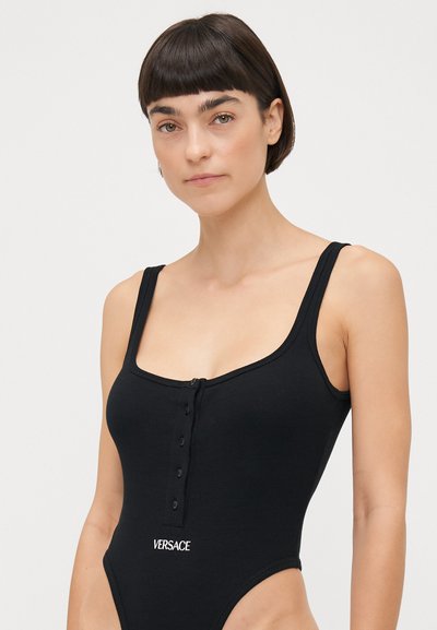 Black one-piece swimsuit in ribbed fabric, featuring a scoop neck, wide straps, front button detail, and white "VERSACE" logo at the waist.