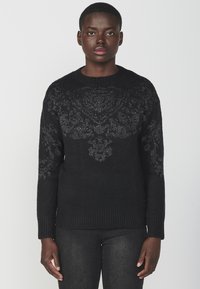 Maglione nero lavorato a maglia con un motivo floreale testurizzato sul petto, colletto rotondo e polsini e orlo a costine. Tessuto morbido.
