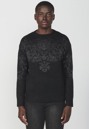Pull en maille noire avec un motif floral texturé sur la poitrine, col rond, et poignets et ourlet côtelés. Tissu doux.