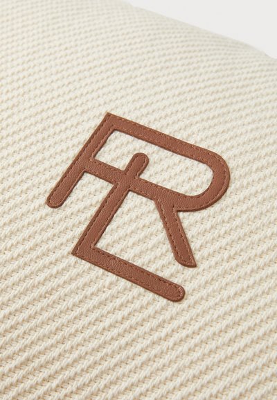 Textúrovaná krémová tkanina s výrazným hnedým koženým logom, ktoré zobrazuje prepletené písmená. Dizajn je minimalisticý a sofistikovaný.