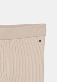 Beige geripptes Strickgewebe mit einem kleinen rechteckigen Tommy Hilfiger Logo-Patch nahe der oberen Kante.