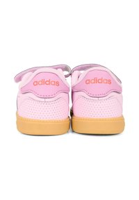 Baskets Adidas roses avec un dessus en cuir perforé, une bande velcro et une semelle en caoutchouc gum contrastante. Logo orange sur les talons.
